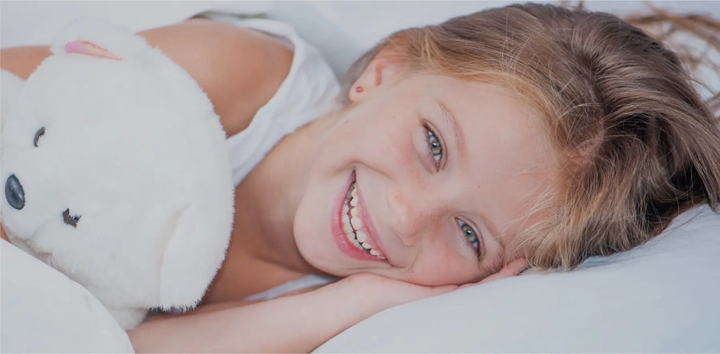 Smiling girl in bed with her favourite white teddy.