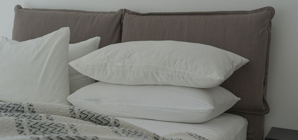 Zoom in shot of the top of a mattress. 4 white fluffy pillows are at the head of the bed. Mattress is on a brown upholstered headboard.