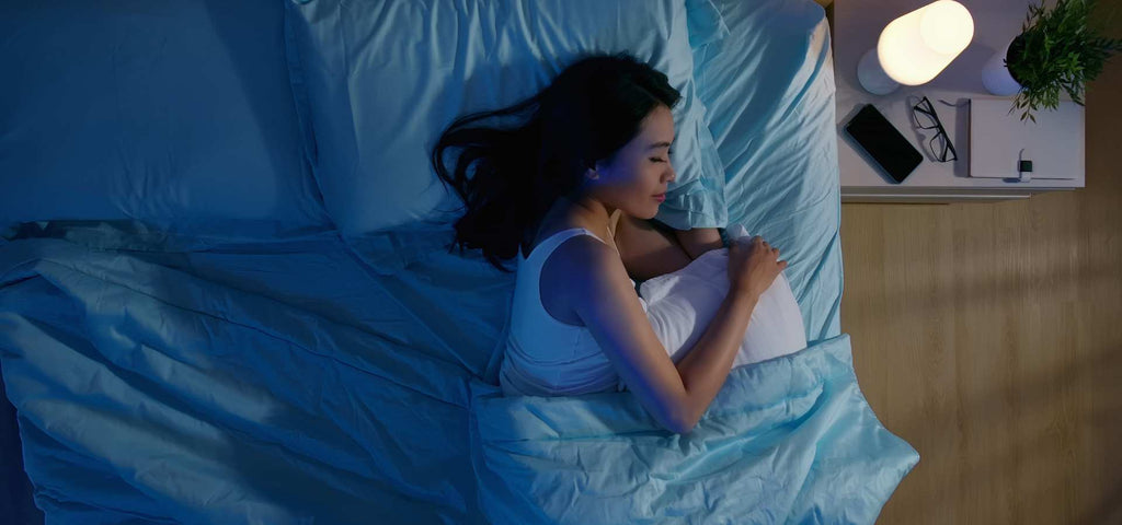 Woman asleep in a dark bedroom with blue sheets on bed