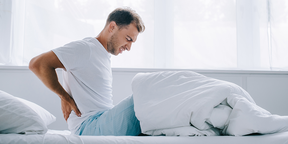 Man waking up holding his lower back in pain
