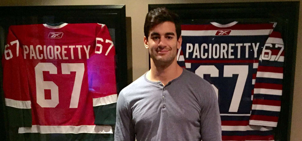 Max Pacioretty standing in front of two of his team jerseys.