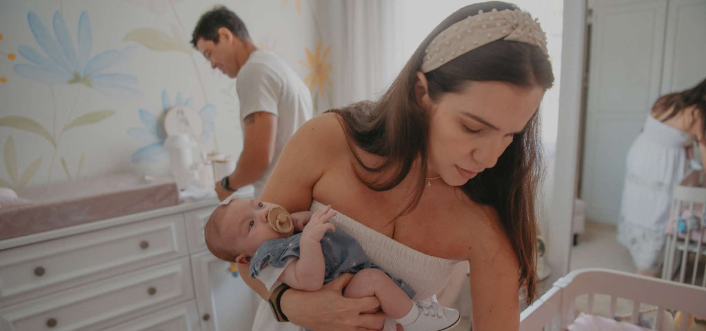 Young mother holding her baby while young father is in the background at the changing table