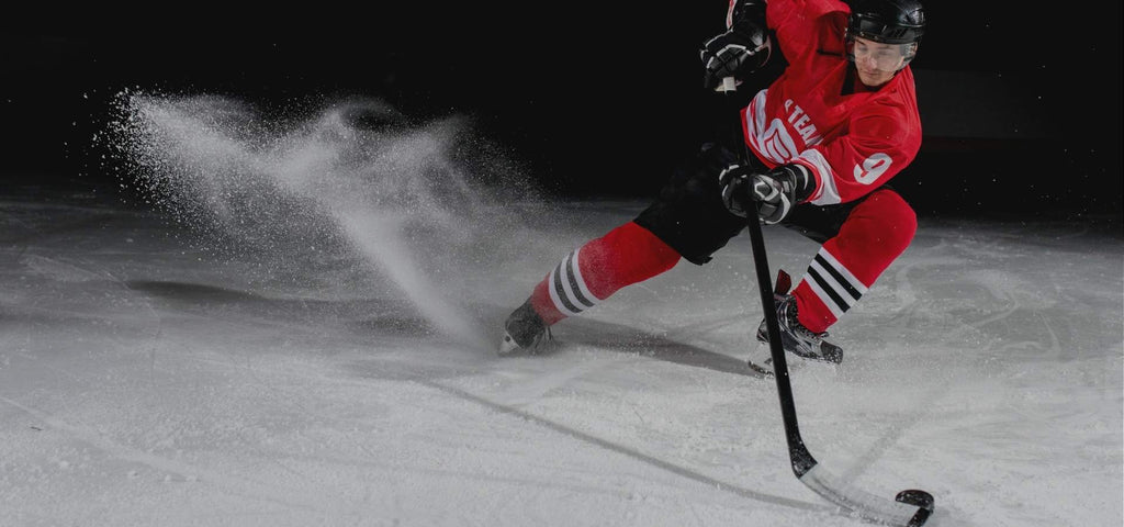 Hockey player wearing a red and black uniform coming to a quick stop to get the hockey puck