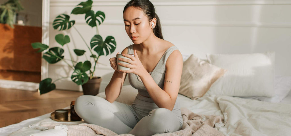 Woman sitting on her bed taking a moment to relax and practice passive wellness 