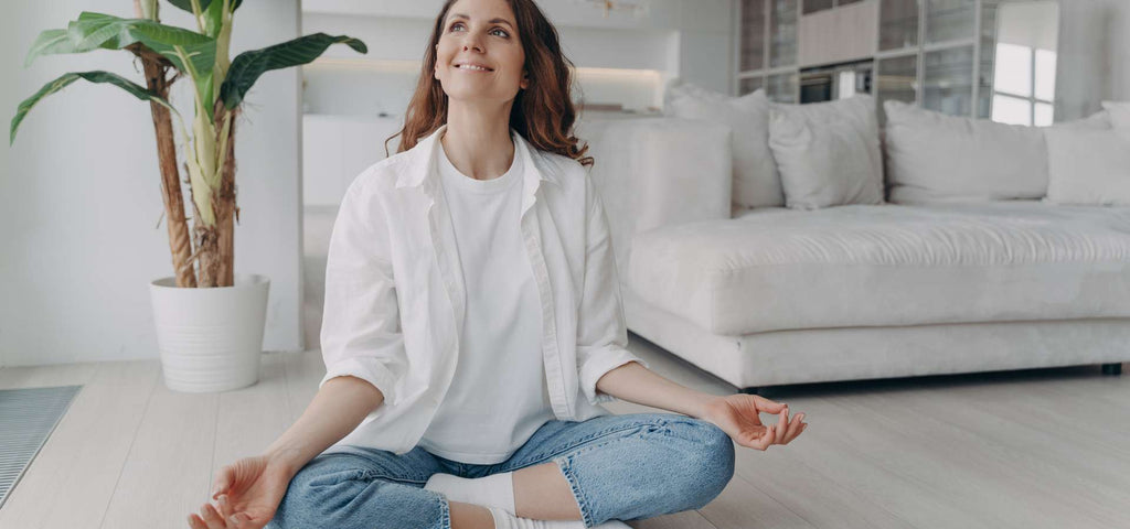 Woman sitting on the floor smiling while meditating.