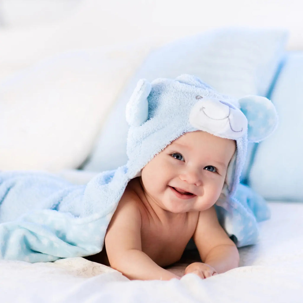Smiling baby on a crib mattress covered with a cute blue bear robe.