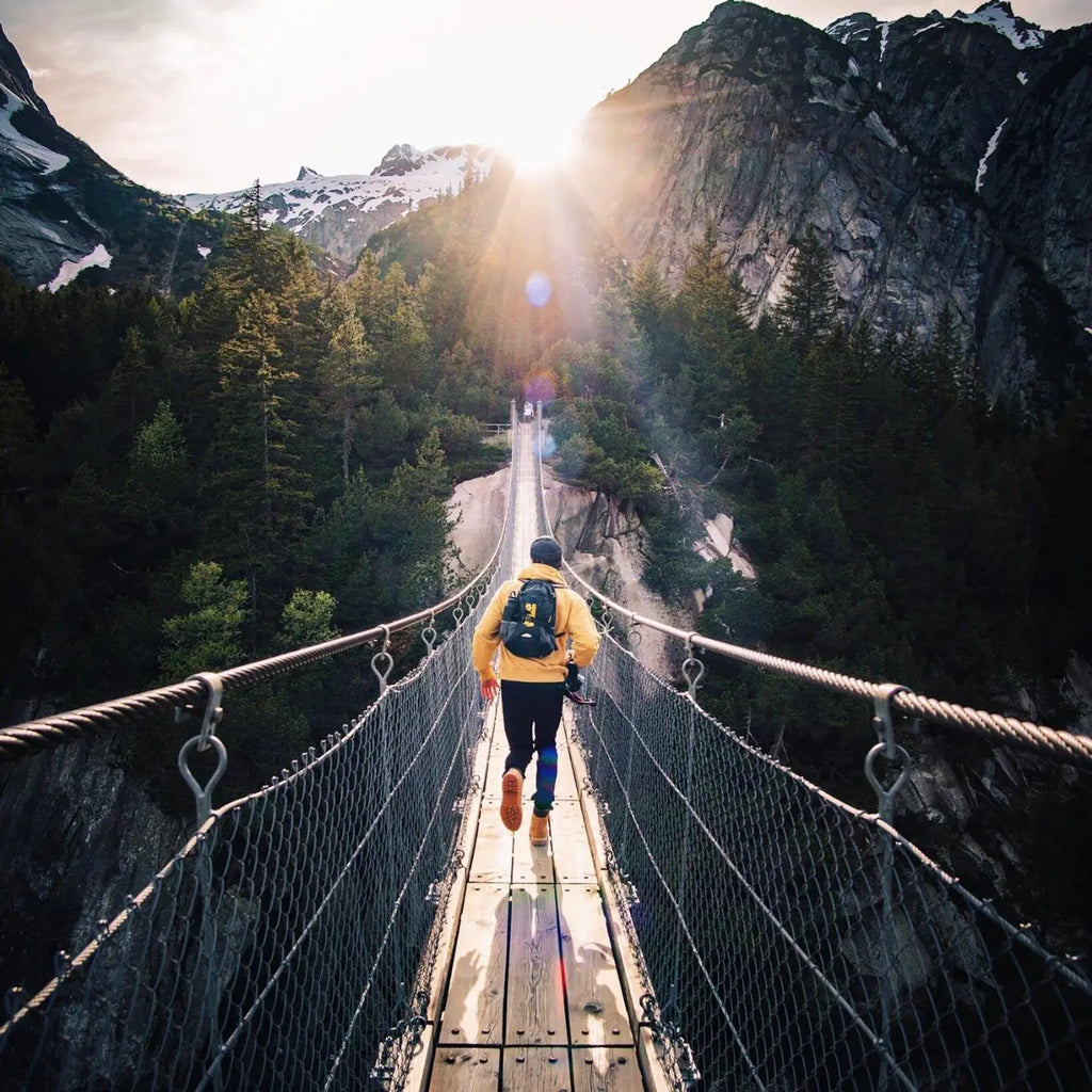 Man in a yellow jacket crossing a rope bridge in the mountains while on a hike